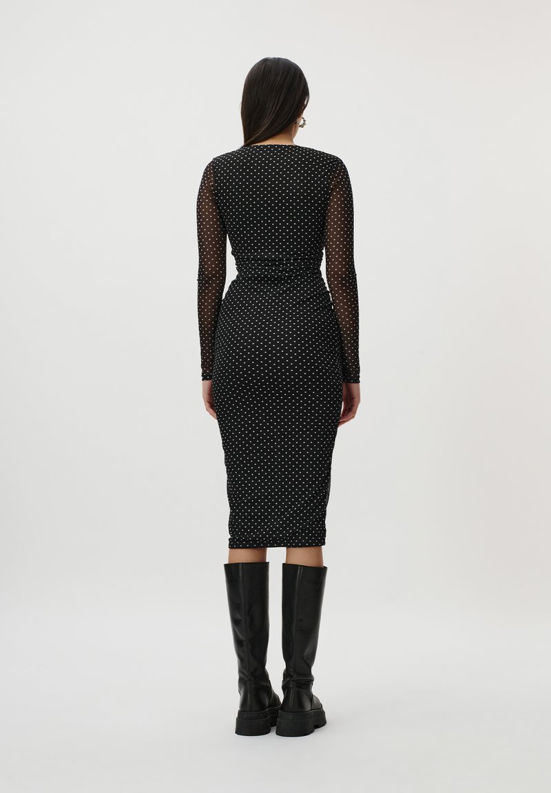 Abito nero a pois con maniche lunghe in tessuto trasparente, silhouette aderente, lunghezza fino al ginocchio. Indossato con stivali neri alti fino al ginocchio. Tessuto a texture liscia.