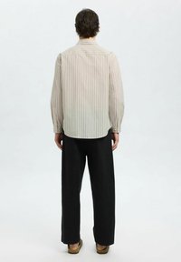 Camicia a maniche lunghe a righe di un beige chiaro, con colletto alla francese e polsini con bottoni, abbinata a pantaloni larghi neri e sandali.