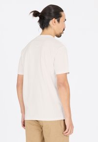 Ljusfärgad bomullströja med korta ärmar, rundad halsringning och en mjuk textur. Synlig sömnad och en avslappnad passform bak.