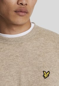 Bežna pletena pulover s rebrastim ovratnikom. Ima majhen črno-rumen logotip orla na levi strani prsnega koša.