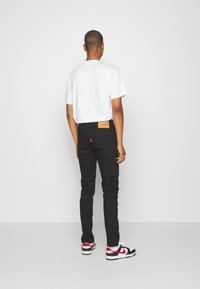 Svarta jeans i denim med en läderlapp och röd detalj, kombinerade med en enkel vit t-shirt och svarta och röda sneakers.