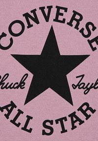 Tissu rose avec un grand motif d'étoile noire au centre, entouré du texte "CONVERSE" et "Chuck Taylor All Star" dans une police en gras.
