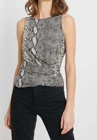 Ärmlös topp i en beige och svart ormskinnstrykt tyg, med en tvistad design vid midjan och en hög krage. Matchas med svarta jeans.