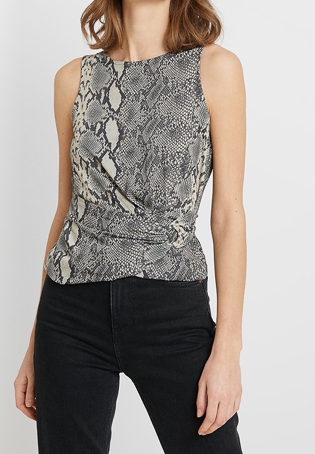 Ärmlös topp i en beige och svart ormskinnstrykt tyg, med en tvistad design vid midjan och en hög krage. Matchas med svarta jeans.