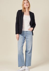 Blazer azul marino con puntos blancos, cierre de un solo botón, combinado con una camiseta blanca, jeans de pierna ancha azul claro y zapatillas blancas.