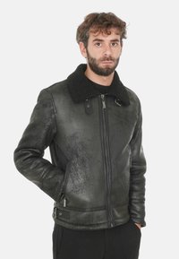 Giacca in pelle nera con una finitura testurizzata, colletto in shearling, chiusura con zip, tasche laterali e dettagli hardware sottili.