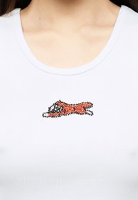 Λευκή ριγωτή μπλούζα με ένα μικρό διακοσμημένο μοτίβο αλεπούς σε πορτοκαλί και μαύρο, τοποθετημένο στο κέντρο κάτω από την κλείδα.