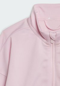 Ljust rosa zip-up jacka med hög krage, texturerad tyg och en liten logodetalj vid nacken. Dragkedjan är tydligt synlig.