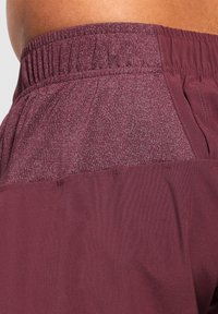 Burgunderfarbene Sportshorts mit einem elastischen Bund, samtiger Textur und einem subtilen Melange-Muster. Enthält Seitentaschen.