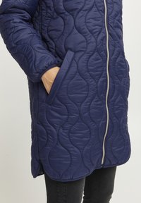 Giacca trapuntata blu navy con motivo a onde, chiusura con zip e tasche laterali. Texture liscia e polsini elasticizzati migliorano la vestibilità e il comfort.
