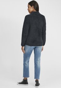 Black, soft, fuzzy pullover with a collar, paired with light blue straight-leg jeans and black high-top sneakers.