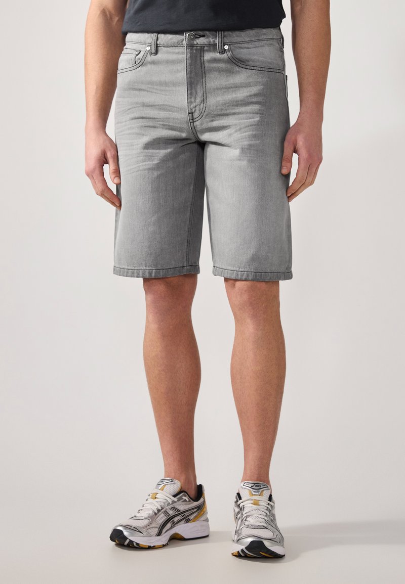 Gray denim shorts with a relaxed fit, knee-length, five-pocket design, and cuffed hems; worn with black and white athletic shoes.