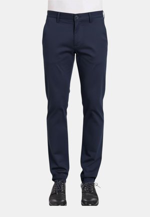 Pantaloni navy a sigaretta con chiusura frontale a bottone e zip, indossati con scarpe eleganti nere in pelle allacciate.