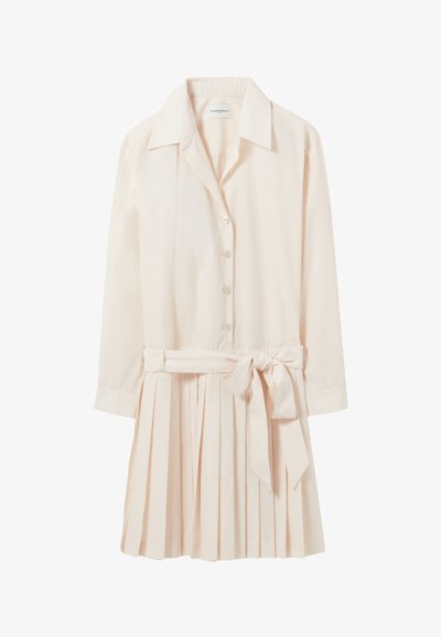 Robe chemise rose clair avec un col, boutons à l'avant, manches longues et jupe plissée. Dispose d'une ceinture amovible à la taille.