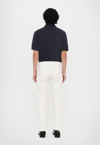 Camisa de polo de manga corta navy combinada con pantalones ajustados blancos y zapatos negros, vista desde atrás. La camiseta tiene cuello y puños.