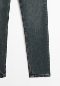 Mörkblå denimjeansben med rak söm och lätt blekning, visade platt på en vit bakgrund.