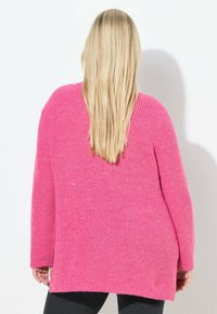 Langärmliger, übergroßer Pullover aus leuchtend pinkem Strick. Verfügt über eine strukturierte Oberfläche und einen abgerundeten Saum, der bis zur Hüfte reicht.