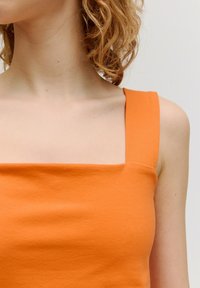 Oranje mouwloze top met een vierkante halslijn, gemaakt van een gladde, zachte stof met een aansluitend ontwerp en brede schouderbanden.