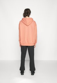 Överdimensionerad hoodie i korallfärgad bomullsblandning, med dragsko i huvan. Kombinerad med svarta vida byxor och kraftiga svarta skor.