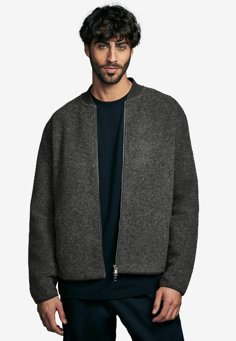 Grijze wollen bomberjack met een ritssluiting, geribbelde kraag en gestructureerd oppervlak. Draagt over een donkerblauw shirt. Casual pasvorm, minimalistisch ontwerp.