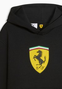 Sweat à capuche noir en tissu doux, arborant un grand logo Ferrari jaune avec un cheval cabré et des accents rayés en haut.