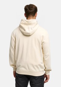 Roomkleurige hoodie met een capuchon met trekkoord, geribbelde manchetten en zoom. Gladde textuur met een losse pasvorm, gecombineerd met donkere jeans.