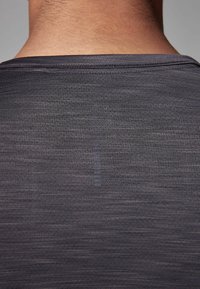 Camisa deportiva negra con una superficie lisa y texturizada; cuenta con un cuello redondo y un sutil detalle de línea en la parte posterior.