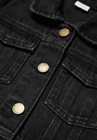 Mustat farkkutakki, jossa on kauluskangas, kultaiset napit, kaksi rintataskua ja teksturoitu kangas. Siisti, jämäkkä ulkoasu.