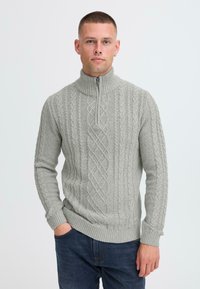 Light gray knitted sweater with a high collar, featuring a cable knit pattern and zip closure. Ribbed cuffs and hem for added texture.