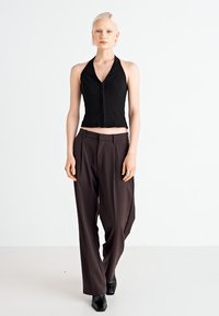 Black halter crop top with a zip front, paired with loose brown trousers and black ankle boots on a model against a plain background.