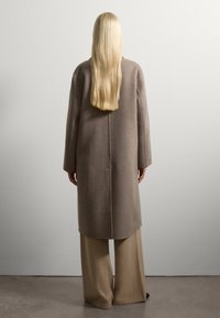 Beige wollen jas met lange mouwen, een losse pasvorm en een rechte zoom. Gecombineerd met beige wijde broek, textuurstof en een minimalistisch ontwerp.