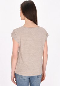 Beige kortærmet top med en struktureret overflade, rund halsudskæring og subtile sømdetaljer på skuldrene. Sammen med blå jeans.