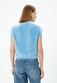 Ärmlös, ljusblå stickad topp med en fluffig textur och hög krage. Matchad med högmidjade urblekta blåjeans.