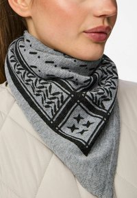 Grå mønstret tørklæde med sorte geometriske designs, der har en trekantet form og blød tekstur, viklet om halsen.