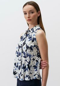 Kwiatowa, bezrękawnikowa bluzka z kołnierzykiem; posiada niebieskie, białe i granatowe wzory na lekkim materiale; zapinana na guziki z przodu; lekko rozkloszowany fason.