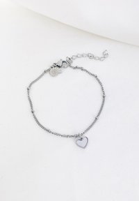 Pulsera de cadena de plata con un pequeño charm en forma de corazón y un cierre tipo langosta, con una cadena de extensión ajustable. Enlaces texturizados y diseño minimalista.