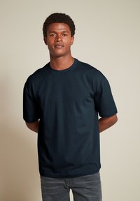 T-shirt di un blu navy scuro con scollatura rotonda, maniche corte e vestibilità morbida. Realizzato in un tessuto liscio, non presenta motivi o dettagli visibili.