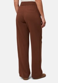 Pantalons marron à jambe large avec une taille élastique et deux poches arrière. Texture lisse, design long jusqu'au sol, adapté pour le port décontracté.