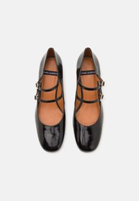 Black patent leather shoes featuring a round toe, two decorative straps with gold buckles, and a smooth brown interior.