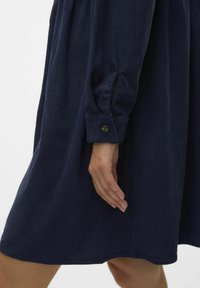 Marineblauwe corduroy jurk met knoopmanchetten, gestructureerde stof en een ontspannen silhouet dat net boven de knie valt.