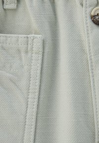 Světle zelená látka s texturovaným vzorem, která má viditelnou kapsu a knoflík s květinovým vzorem.