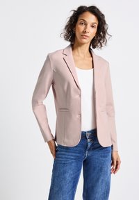 Blazer rose clair avec revers structurés, deux poches avant et coupe slim, associé avec un haut blanc et un jean en denim bleu. Texture lisse.
