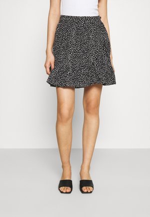 Black skirt with white polka dots, ruffled hem, worn with white top and black open-toe slip-on shoes, shown from waist to feet.