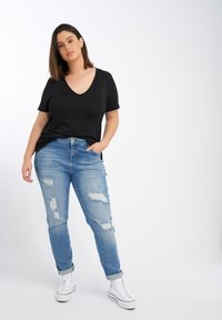Zwarte V-hals t-shirt gecombineerd met lichtblauwe versleten jeans. De jeans hebben scheuren en opgerolde boorden, aangevuld met witte sneakers.