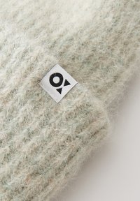 Light green knit wool beanie with a textured surface and a small white label featuring a black logo sewn on the side.