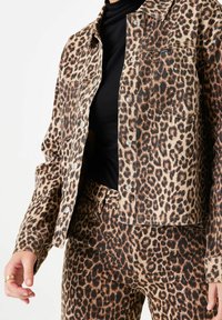 Leopardmönstrad denimjacka och matchande byxor, med en beige bakgrund, mörkbruna fläckar, knäppningar framtill och fickor.