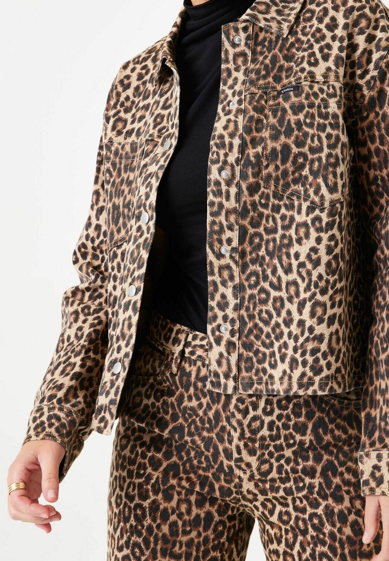 Leopardmönstrad denimjacka och matchande byxor, med en beige bakgrund, mörkbruna fläckar, knäppningar framtill och fickor.