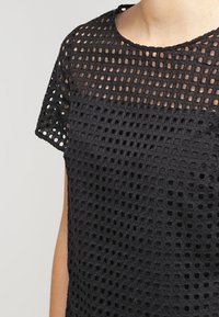 Top negro con un diseño de malla texturizada, de manga corta y cuello redondo. La tela tiene un patrón abierto en forma de rejilla.