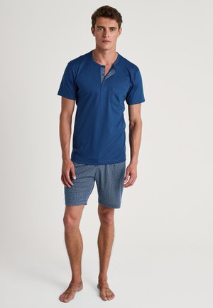 Chemise à manches courtes, bleu marine, avec une patte de boutonnage et une poche à motifs, associée à un short bleu à motifs. Les deux sont en tissu léger.