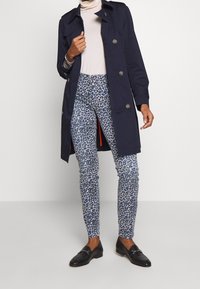 Námornícký trenčkot se stříbrnými knoflíky, v kombinaci s módními modrými kalhotami s potiskem zvířat. Černé mokasíny dotvářejí celkový vzhled. Hladké látky, střižený střih.